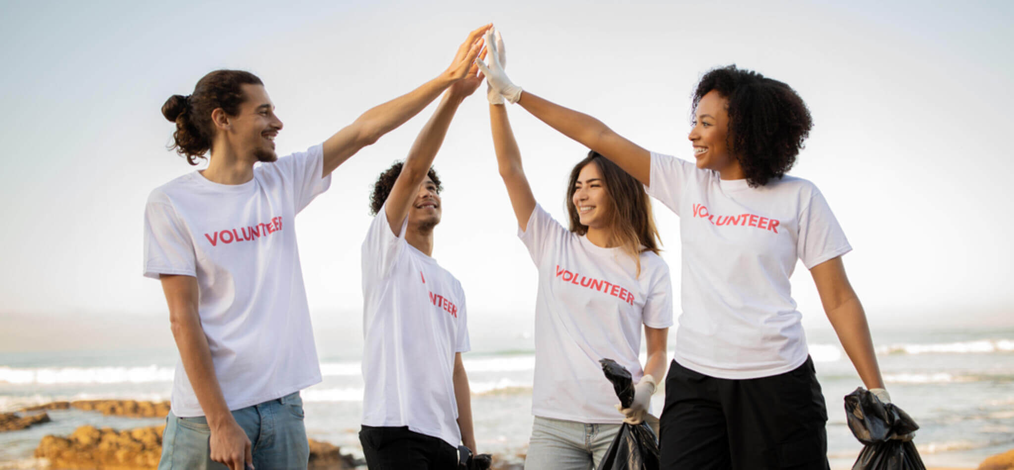Four volunteers high-fiving on a beach holding trash bags.